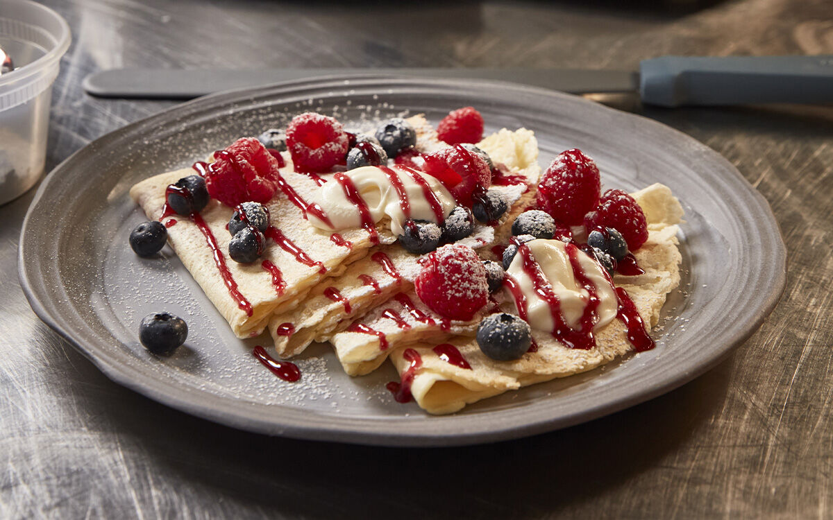 A plate with folded crepes, berries, and sauce.